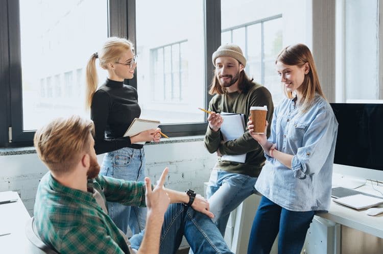 Junges Team in lockerer Arbeitskultur: Payroll in modernen Unternehmen Vier junge Kolleg:innen im Büro tauschen sich informell aus – Symbolbild für moderne Arbeitsmodelle und HR-Prozesse