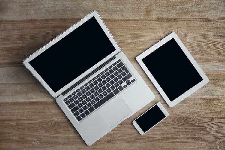 Laptop, Tablet und Smartphone – digitale Arbeitsmittel in der Lohnbuchhaltung Ein silberner Laptop, ein Tablet und ein Smartphone liegen auf einem Holztisch. Die Bildkomposition zeigt moderne digitale Geräte, die häufig in der Lohnbuchhaltung verwendet werden.