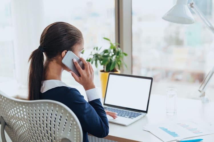 Mitarbeiterin in der Lohnbuchhaltung telefoniert und arbeitet am Laptop Frau sitzt am Schreibtisch, telefoniert und arbeitet am Laptop – typischer Arbeitsalltag in der Lohnbuchhaltung