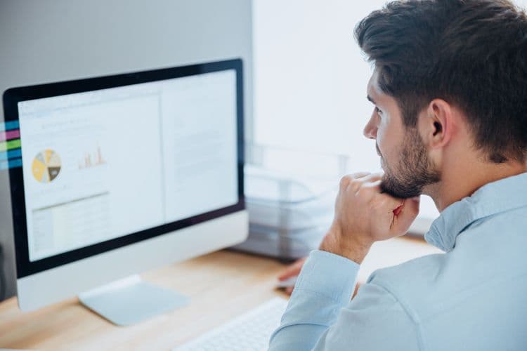Junger Mann analysiert Daten und Diagramme am Computer im Büro Ein junger Mann sitzt an einem Schreibtisch und betrachtet konzentriert Diagramme und Statistiken auf einem großen Monitor – Symbolbild für Datenanalyse, Controlling oder Business Intelligence