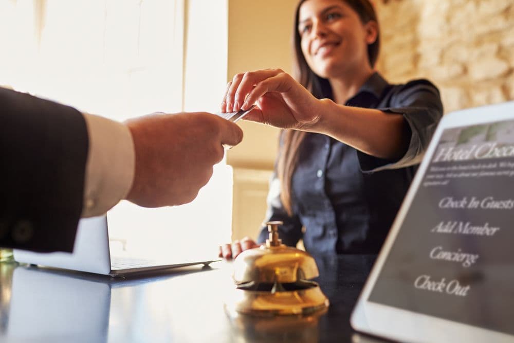 Hotelmitarbeiterin am Empfang – Lohnabrechnung und Arbeitszeiterfassung im Gastgewerbe Eine Hotelangestellte am Empfang übergibt einer Person eine Zimmerkarte – Symbolbild für Lohnabrechnung, Arbeitszeiten und Schichtplanung im Gastgewerbe