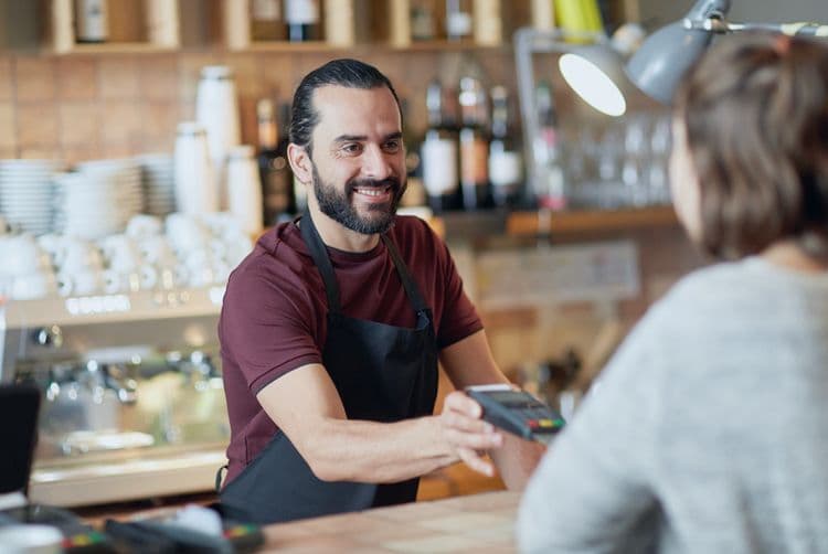 Lohnabrechnung im Gastgewerbe: Minijobs und flexible Beschäftigungsmodelle Servicekraft reicht Kundin ein Kartenlesegerät im Café – Symbol für Minijob und Abrechnung im Gastgewerbe