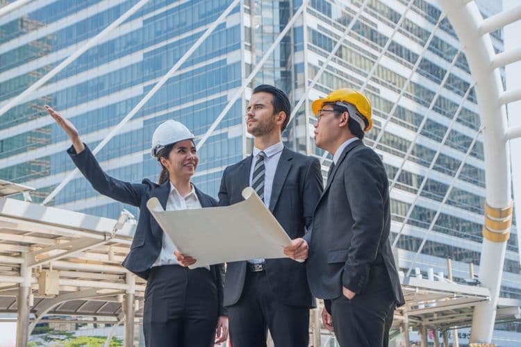 Projektplanung und Lohnabrechnung im Baugewerbe Team aus Bauleiterin und Projektverantwortlichen bespricht Bauplan vor moderner Büroarchitektur