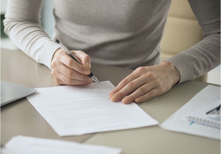 Unterschrift auf Arbeitsvertrag: Relevanz für die Lohnbuchhaltung Person unterschreibt ein Dokument am Schreibtisch – Symbol für Arbeitsvertrag oder Personalunterlagen