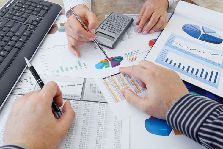 Analyse von Lohndaten und Abrechnungsdiagrammen im Unternehmen Hände von Mitarbeitenden bei der Analyse von Lohnabrechnungsdaten mit Diagrammen, Taschenrechner und Stift auf einem Schreibtisch