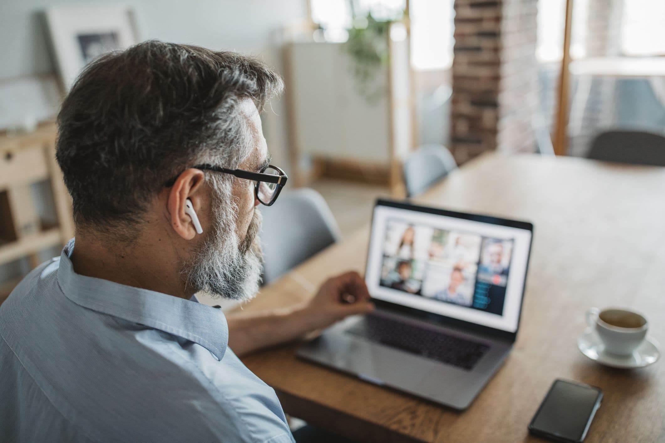 Lohnbuchhaltung remote: Teilnahme an einem Payroll-Webinar im Homeoffice Mann mit Kopfhörern nimmt im Homeoffice an einem Online-Meeting auf dem Laptop teil