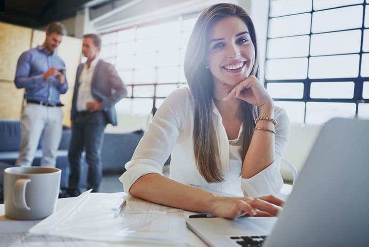 Digitale Lohnabrechnung im Büro: Effizient, modern und mitarbeiterfreundlich Junge Frau im modernen Büro lächelt am Laptop – Symbol für digitale Lohnbuchhaltung und HR-Zufriedenheit