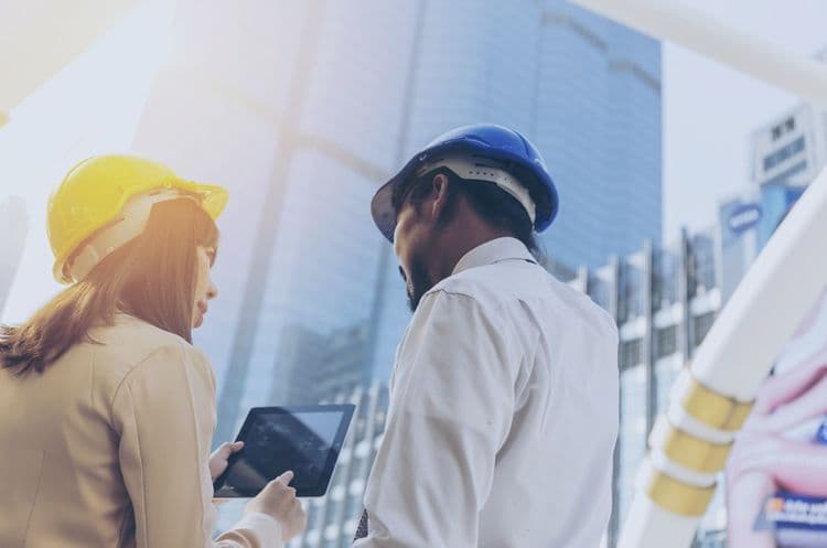 Digitale Lohnabrechnung auf der Baustelle: Baulohn effizient verwalten Zwei Bauverantwortliche mit Schutzhelmen besprechen auf der Baustelle Daten auf einem Tablet