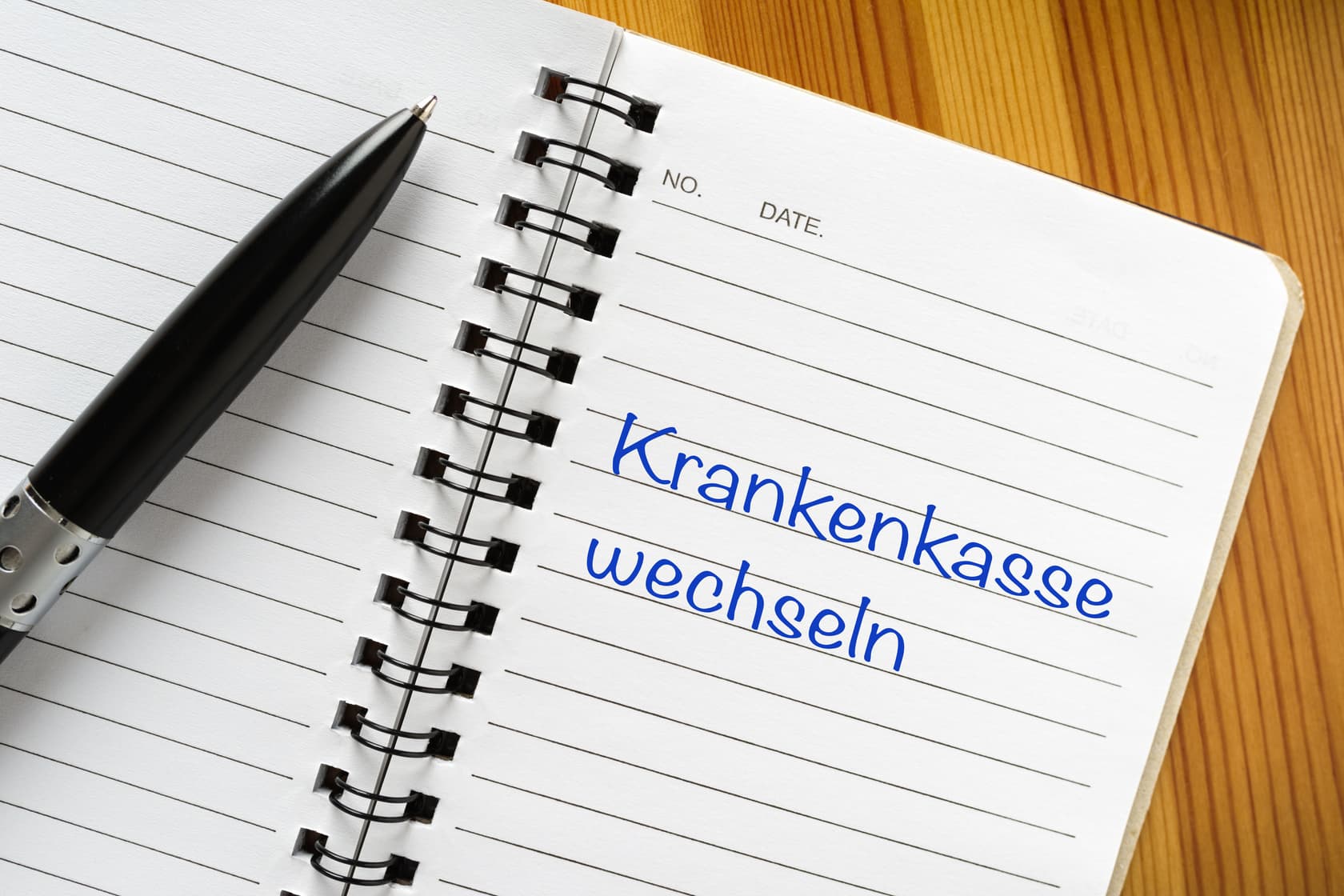 Krankenkassenwechsel richtig melden: Was die Lohnbuchhaltung beachten muss Notizbuch mit der Aufschrift „Krankenkasse wechseln“ und Kugelschreiber auf Holztisch