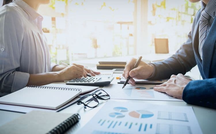 Zwei Personen analysieren Lohnabrechnungsdaten am Schreibtisch Geschäftspersonen besprechen Lohnabrechnungsunterlagen mit Taschenrechner und Statistiken – Symbolbild für Lohnbuchhaltung und Gehaltsabrechnung