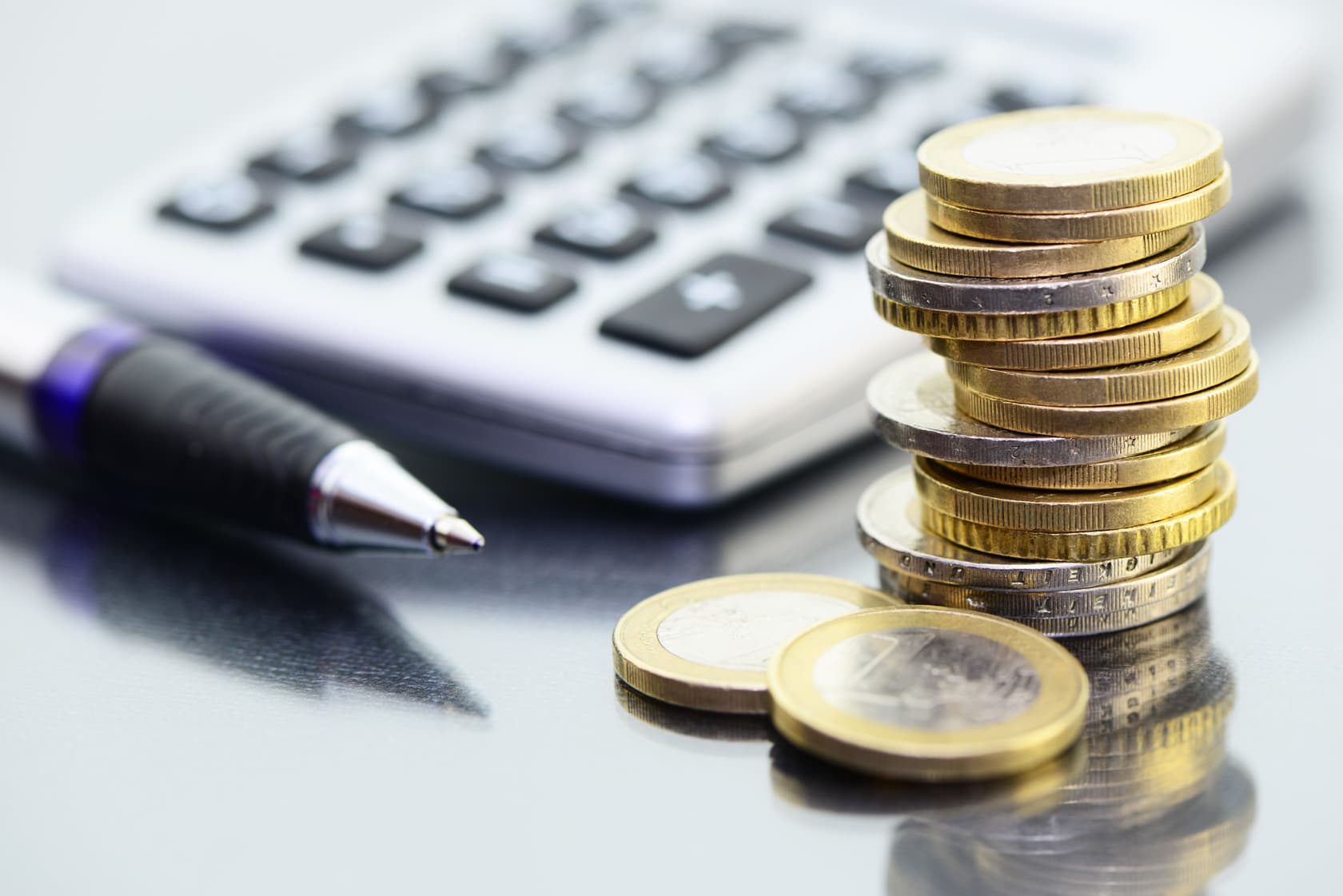 Euro-Münzen mit Taschenrechner und Kugelschreiber – Finanzberechnungen in der Lohnbuchhaltung Gestapelte Euro-Münzen liegen neben einem Kugelschreiber und einem Taschenrechner auf einem glänzenden Tisch. Symbol für Gehaltsabrechnung, Lohnkosten und präzise Kalkulation in der Lohnbuchhaltung.