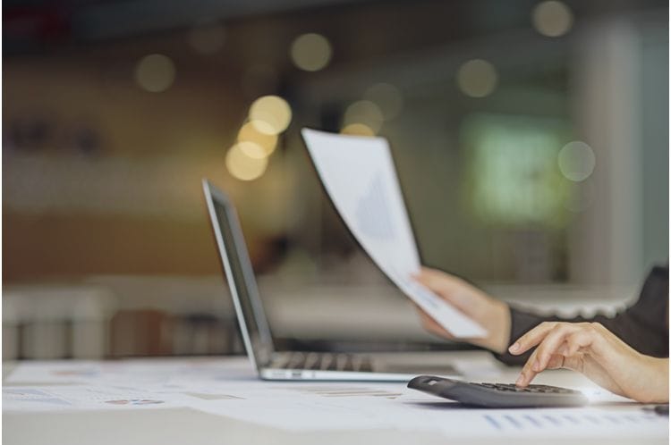 Lohnbuchhaltung am Computer: effiziente Lohn- und Gehaltsabrechnung Eine Person im Büro bearbeitet die Lohnbuchhaltung am Laptop und prüft mit einem Taschenrechner Zahlen für die Gehaltsabrechnungen.