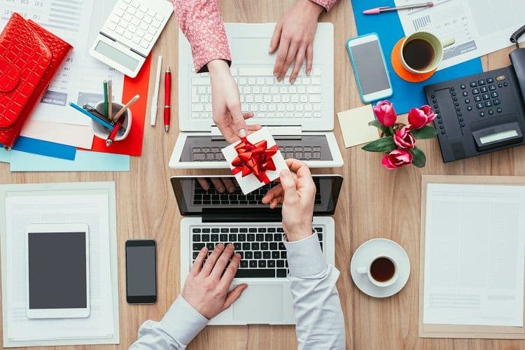 Mitarbeitergeschenke steuerfrei: Sachzuwendungen korrekt abrechnen Zwei Personen überreichen sich ein Geschenk über ihren Laptops – Symbol für steuerfreie Sachzuwendungen im Büro